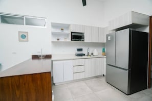 A modern kitchen with white cabinetry, a stainless steel refrigerator, and a microwave. - Casa Swell at Costa Lofts (Jaco)