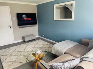 A living room with a flat-screen TV displaying Netflix, a sofa, a coffee table, and a mirror on the wall. - COSY HOME - KINGSIZE BED & PRIVATE PARKING (Saughall Massie)