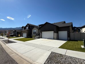 A residential street with modern houses, a clear sky, and a mountain range in the background. - Mountain Green Getaway - Home Theater Room - Backyard Hot tub and Firepit (Mountain Green)