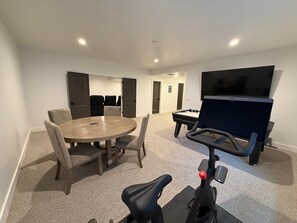 A room with a round table, chairs, a treadmill, a TV, and a door. - Mountain Green Getaway - Home Theater Room - Backyard Hot tub and Firepit (Mountain Green)