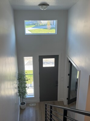 A hallway with a dark door, a potted plant, and a view of a green landscape through a window. - Mountain Green Getaway - Home Theater Room - Backyard Hot tub and Firepit (Mountain Green)