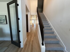A modern interior with a staircase, wooden flooring, and a hallway leading to a room with a bed. - Mountain Green Getaway - Home Theater Room - Backyard Hot tub and Firepit (Mountain Green)