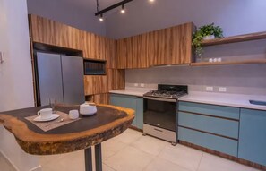 A modern kitchen with wooden cabinetry, a built-in oven, and a dining area with a wooden table. - Casa Aurelia | Cozy Stay with AC and Parking (Oaxaca de Juárez)