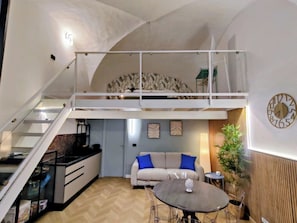 A loft-style apartment with a mezzanine, a kitchenette, a dining area, and a living room with a sofa and a clock on the wall. - Naumachia77 In the heart of Catania’s historic center, where nightlife meets culture. (Catania)