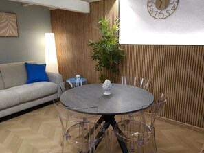 A modern dining area with a round table, clear chairs, a potted plant, a clock, and a sofa with a blue pillow. - Naumachia77 In the heart of Catania’s historic center, where nightlife meets culture. (Catania)