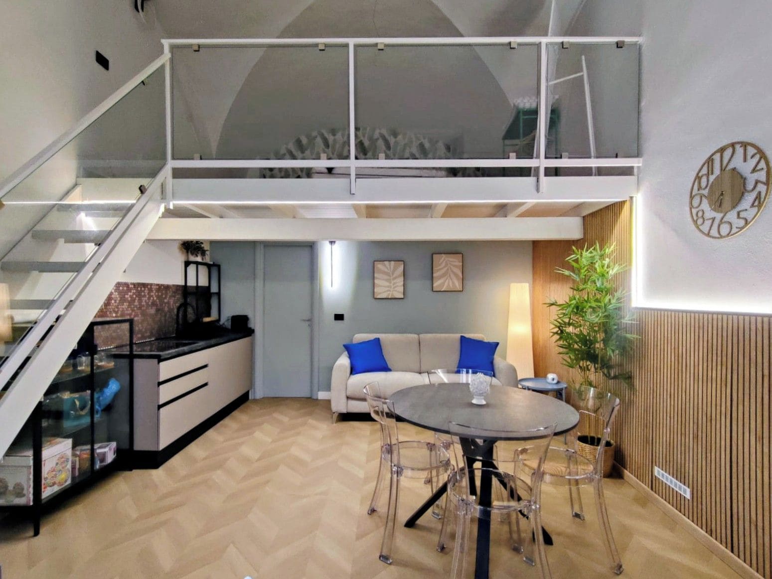 A modern interior with a dining area, sofa, staircase, and a wall clock.