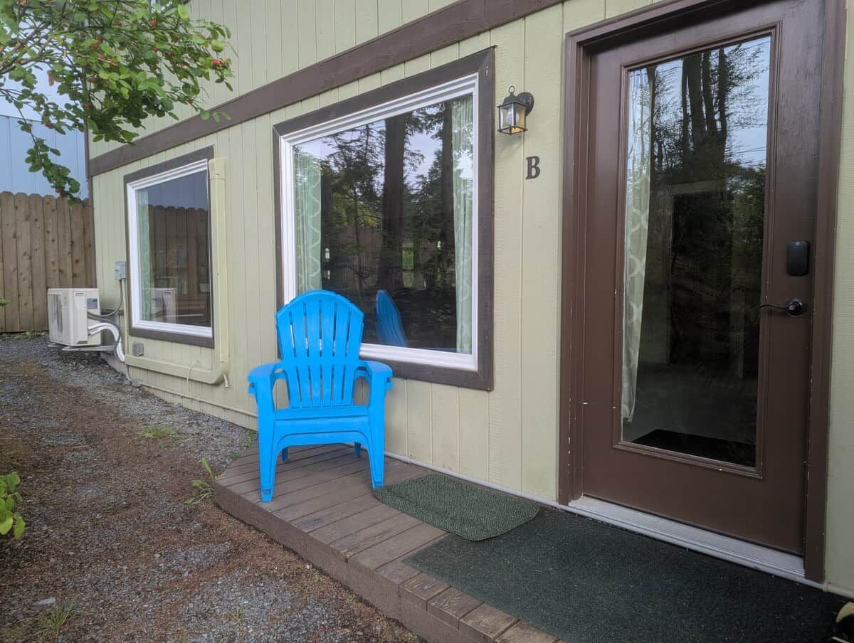 A building with a brown door, a blue chair outside, and a wooden deck.