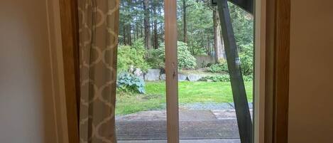 A view through a sliding glass door into a backyard with a wooden deck, a grassy area, and trees.