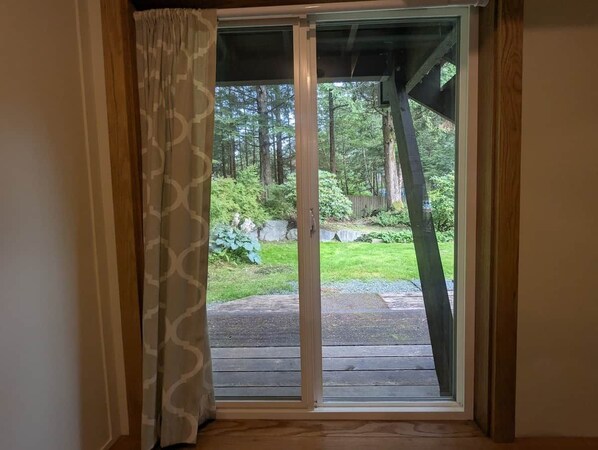A view through a sliding glass door into a backyard with a wooden deck, a grassy area, and trees.