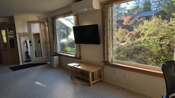 Una habitación con un ventanal grande, un televisor de pantalla plana montado en la pared, un banco de madera y una puerta que da a otra habitación.
