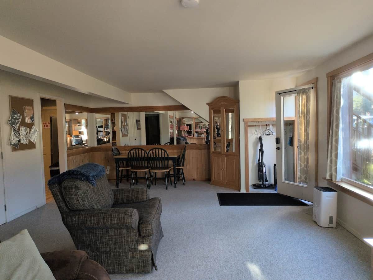 A spacious living area with a dining table and chairs, a sofa, and a large window.