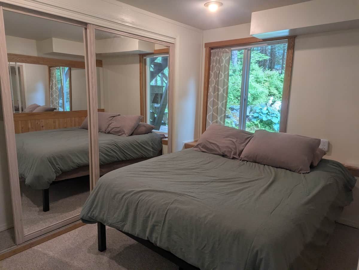 Un dormitorio con dos camas, un espejo grande y una ventana con vistas a zonas verdes.