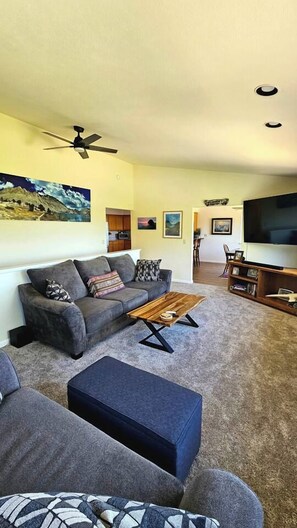 A living room with a sofa, ottoman, coffee table, TV, and ceiling fan. - The Ranch Near the River- Hot tub -outdoor dining (Nevada City)