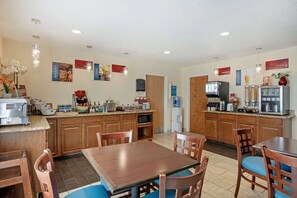 A hotel kitchen with wooden cabinets, a dining table with chairs, and various kitchen appliances. - Best Western Plus Lonoke 2 Queen Studio (Lonoke)