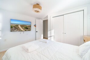 Un dormitorio con cama, televisor montado en la pared, una puerta y una lámpara en el techo.
