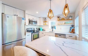 Eine moderne Küche mit einem Edelstahl-Kühlschrank, einer Mikrowelle, einem Backofen und einer großen Marmor-Kochinsel.