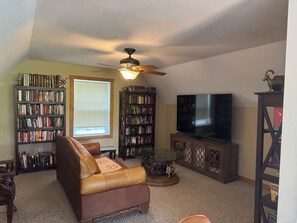 Ein Wohnzimmer mit einem braunen Ledersofa, zwei Bücherregalen, einem Glastisch und einem Deckenventilator.