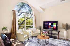 A living room with a large window, a television, a sofa, a coffee table, and a potted plant. - Beach-Entry Pool Mini-Golf FirePit SeaWorld & BMT (San Antonio)