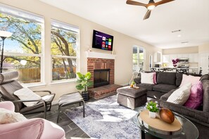 A modern living room with a fireplace, a flat-screen TV mounted above it, and a dining area in the background. - Beach-Entry Pool Mini-Golf FirePit SeaWorld & BMT (San Antonio)