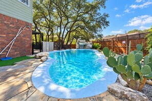 A swimming pool with a stone border, surrounded by a brick wall, trees, and a cactus plant. - Beach-Entry Pool Mini-Golf FirePit SeaWorld & BMT (San Antonio)