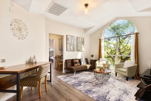 A spacious living room with a dining area, a large window with a view of trees, and a cozy seating arrangement. - Beach-Entry Pool Mini-Golf FirePit SeaWorld & BMT (San Antonio)