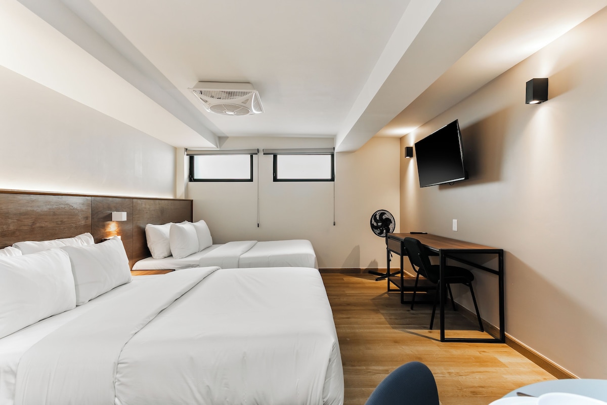 Habitación de hotel con dos camas, un escritorio, una silla, un televisor y un ventilador de techo.