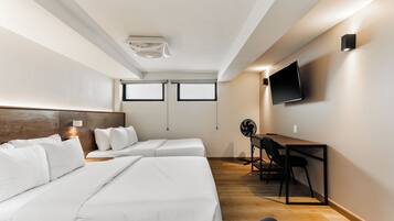 Ein Hotelzimmer mit zwei Betten, einem Schreibtisch, einem Sessel, einem Fernseher und einem Deckenventilator.