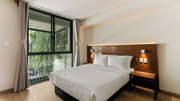 A bedroom with a large bed, a nightstand, a wall-mounted lamp, and a window with curtains.
