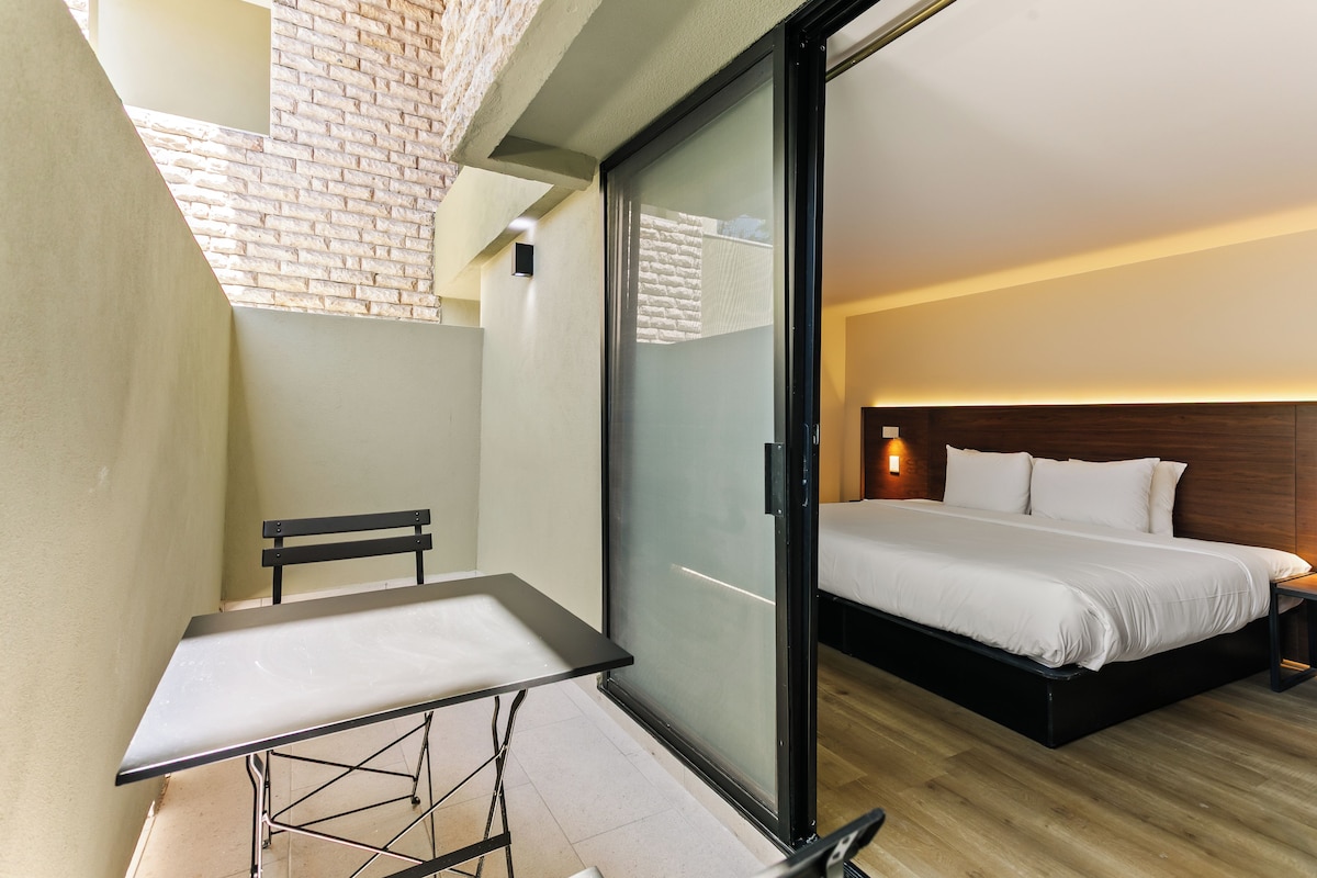 Habitación de hotel con una cama, una mesita pequeña y un banco.