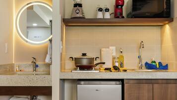 A compact kitchen with a built-in dishwasher, a microwave, a blender, and a kettle on the countertop.