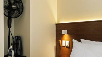 Une chambre d’hôtel comprenant un lit, une table de chevet, une lampe fixée au mur, une prise de courant et un ventilateur suspendu.