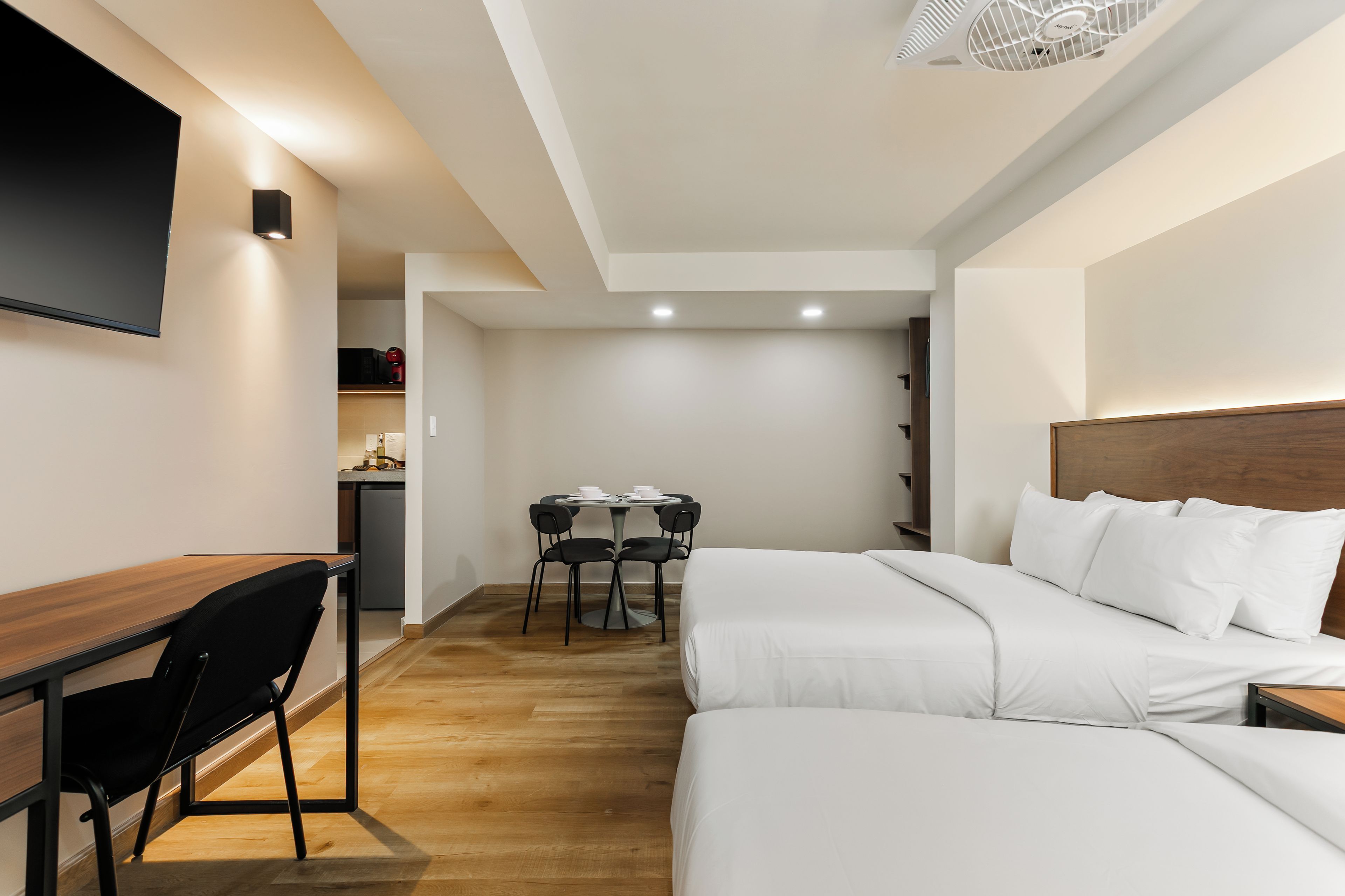 Una habitación de hotel con cama, escritorio, silla, una mesa con tazas y un microondas.