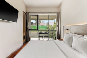 A hotel room with a bed, a TV mounted on the wall, a balcony with a table and chairs, and a view of the cityscape. - Hierba By Homirent  (Santiago de Querétaro)