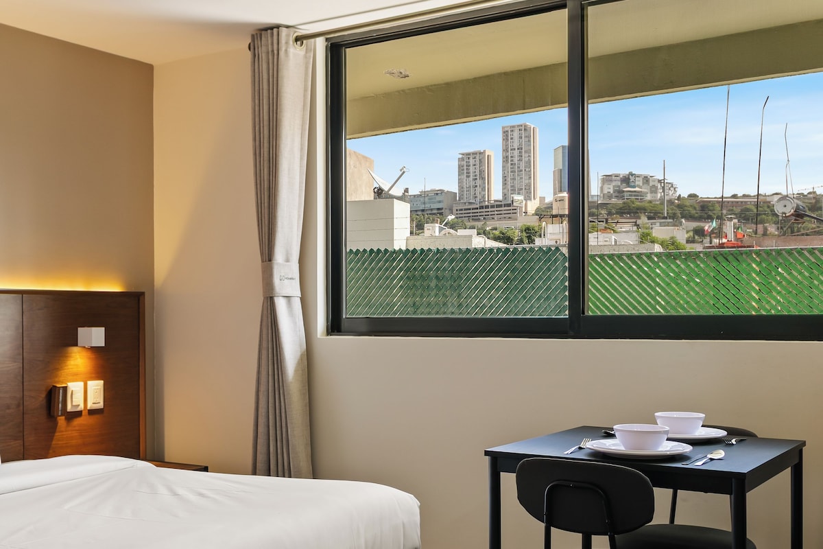 Habitación de hotel con cama, escritorio y ventana con vista a la ciudad.