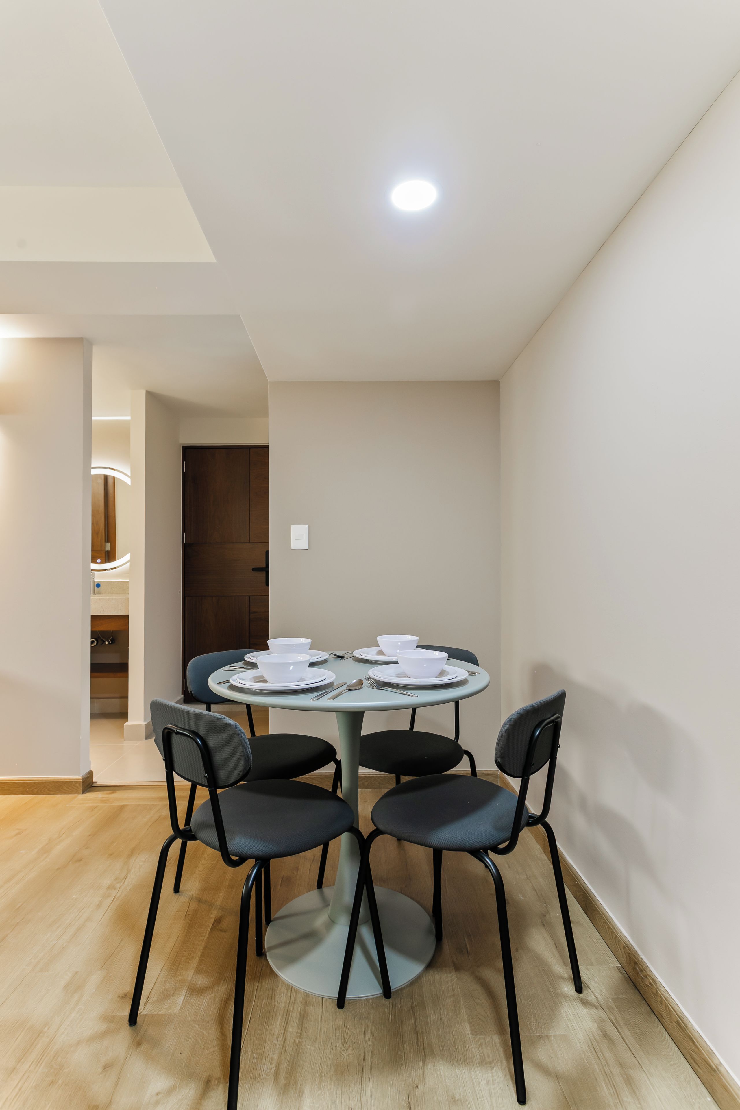 A dining area with a round table, four chairs, and a light fixture on the ceiling.