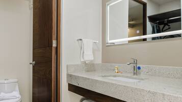 Ein Badezimmer mit Holztür, Toilette in Weiß, Waschbecken mit Spiegel und Handtuchhalter.
