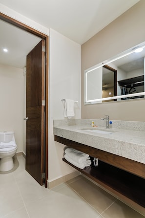 Un baño con puerta de madera, inodoro blanco, lavamanos con espejo y un perchero para toallas.