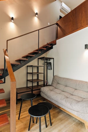 Un interior moderno con una escalera de madera, un sofá gris y una mesa redonda negra.