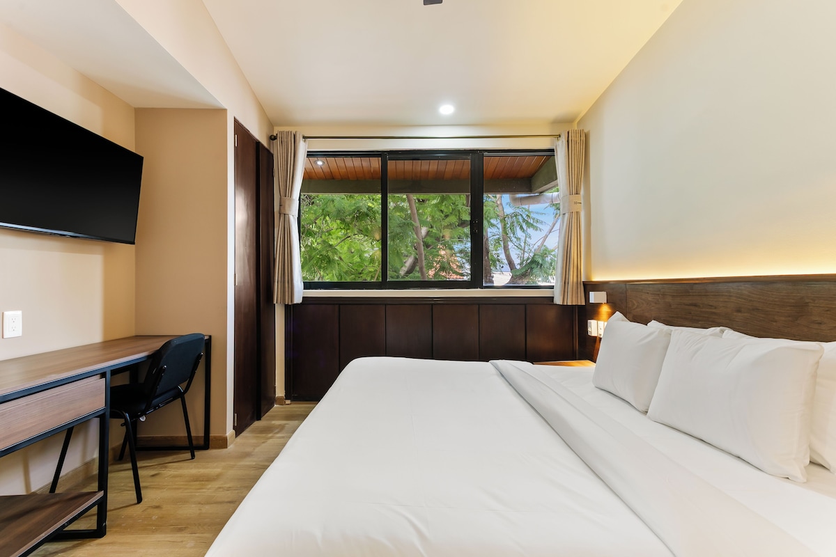 Una habitación de hotel con cama, escritorio y ventana con vistas a árboles.
