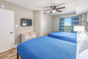 A hotel room with two beds, a ceiling fan, a TV, a window with curtains, and a bedside lamp. - Spacious 3BR Coastal Getaway at Sand Dunes (Myrtle Beach)