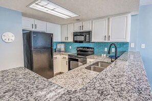 A kitchen with white cabinets, a stainless steel refrigerator, a microwave, a stove, and a sink with a granite countertop. - Spacious 3BR Coastal Getaway at Sand Dunes (Myrtle Beach)