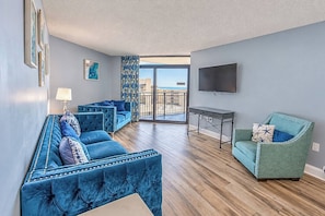 A modern living room with a blue sofa set, a green armchair, and a flat-screen TV mounted on the wall. - Spacious 3BR Coastal Getaway at Sand Dunes (Myrtle Beach)