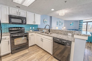 A modern kitchen with white cabinets, a black stove, and granite countertops. - Spacious 3BR Coastal Getaway at Sand Dunes (Myrtle Beach)