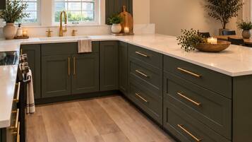 A modern kitchen with dark green cabinets, gold handles, a marble countertop, and pendant lighting.