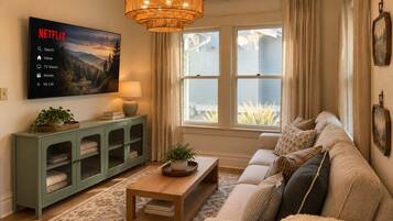 A living room with a sofa, a coffee table, a cabinet with glass doors, a television mounted on the wall, and a window with curtains.