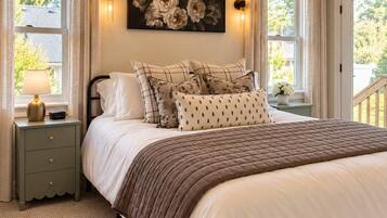 A bedroom with a bed, nightstand, lamp, wall art, and windows.