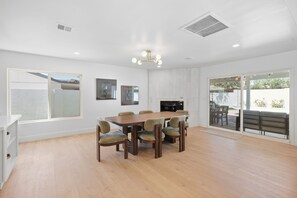 A spacious dining area with a wooden table and chairs, a modern chandelier, and a view through a glass door to an outdoor patio. - Desert Sonrisa - Scottsdale Modern Home 3BR Pool (Scottsdale)
