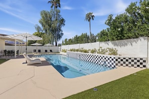 A swimming pool with checkered tiles, surrounded by a white wall and a grassy area with lounge chairs and umbrellas. - Desert Sonrisa - Scottsdale Modern Home 3BR Pool (Scottsdale)