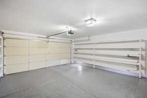 Ett garage med en stängd garagedörr, en projektor som är monterad i taket och vita hyllsystem.