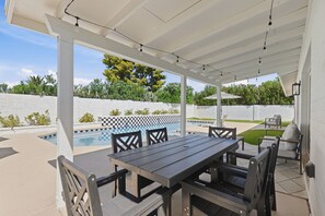 Een terras buiten met een zwembad, een tafel en stoelen, en een overdekte zithoek.